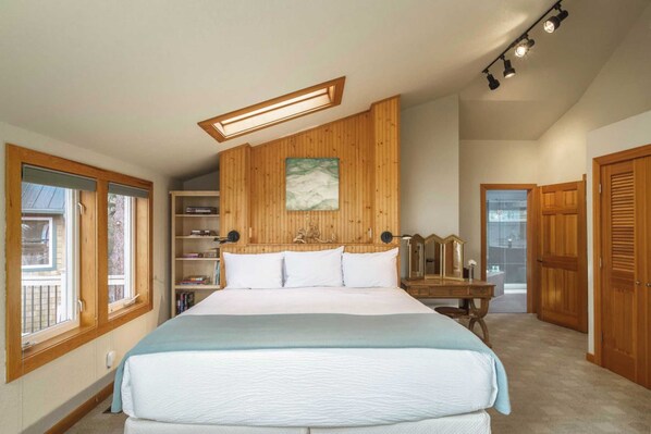 A bedroom with a large bed, wooden panel walls, a skylight, a bookshelf, and a wooden dresser.