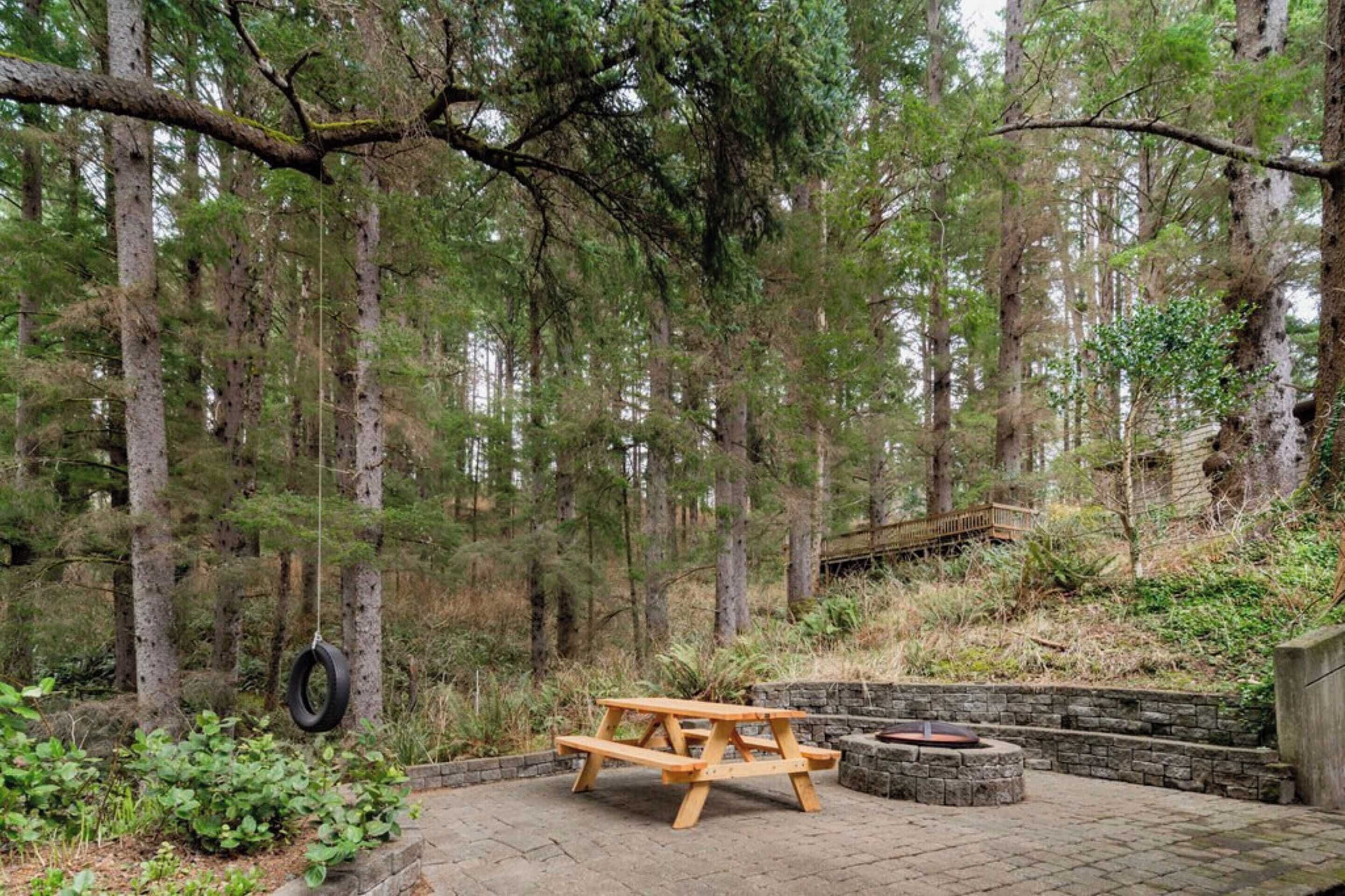 A picnic table in a forested area with a stone fire pit nearby.