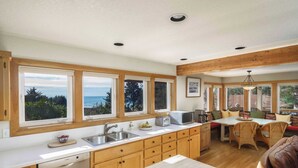 A kitchen with wooden cabinets, a dishwasher, a sink, and a dining area with a table and chairs. - Coastal Getaway in Manzanita w Fire Pit, Guest House & Views Seagrove by Avantstay (Manzanita)