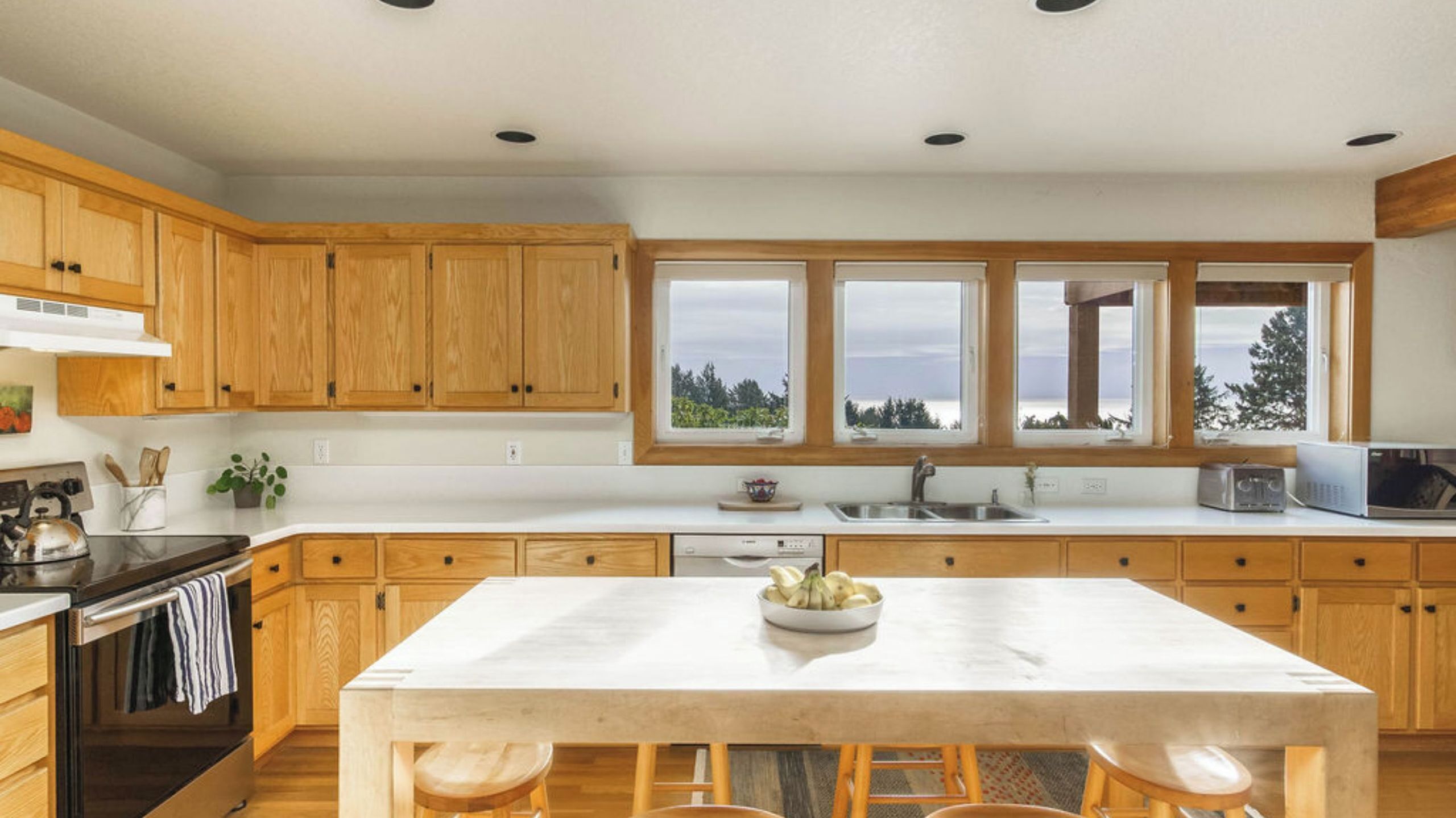 A modern kitchen with wooden cabinets, a large island, and a view of the outdoors.