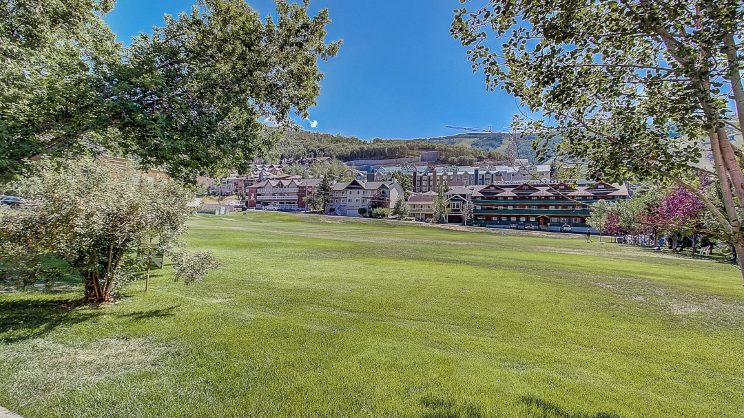 A hotel with a large lawn in front, multiple buildings in the background, and a clear blue sky.