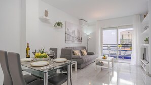 Un soggiorno moderno con tavolo da pranzo in vetro, divano grigio e un balcone con vista.