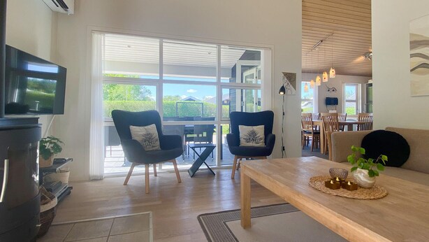 A modern living room with a TV, two armchairs, a wooden table, and a large window offering a view of the outdoors. - Amazing home in Hals with kitchen (Hals)