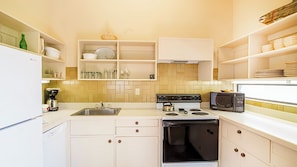 A kitchen with white cabinets, a stove, a microwave, and shelves with dishes and jars. - Telluride Lodge 305 by Avantstay Close to Slopes & Town! (Telluride)
