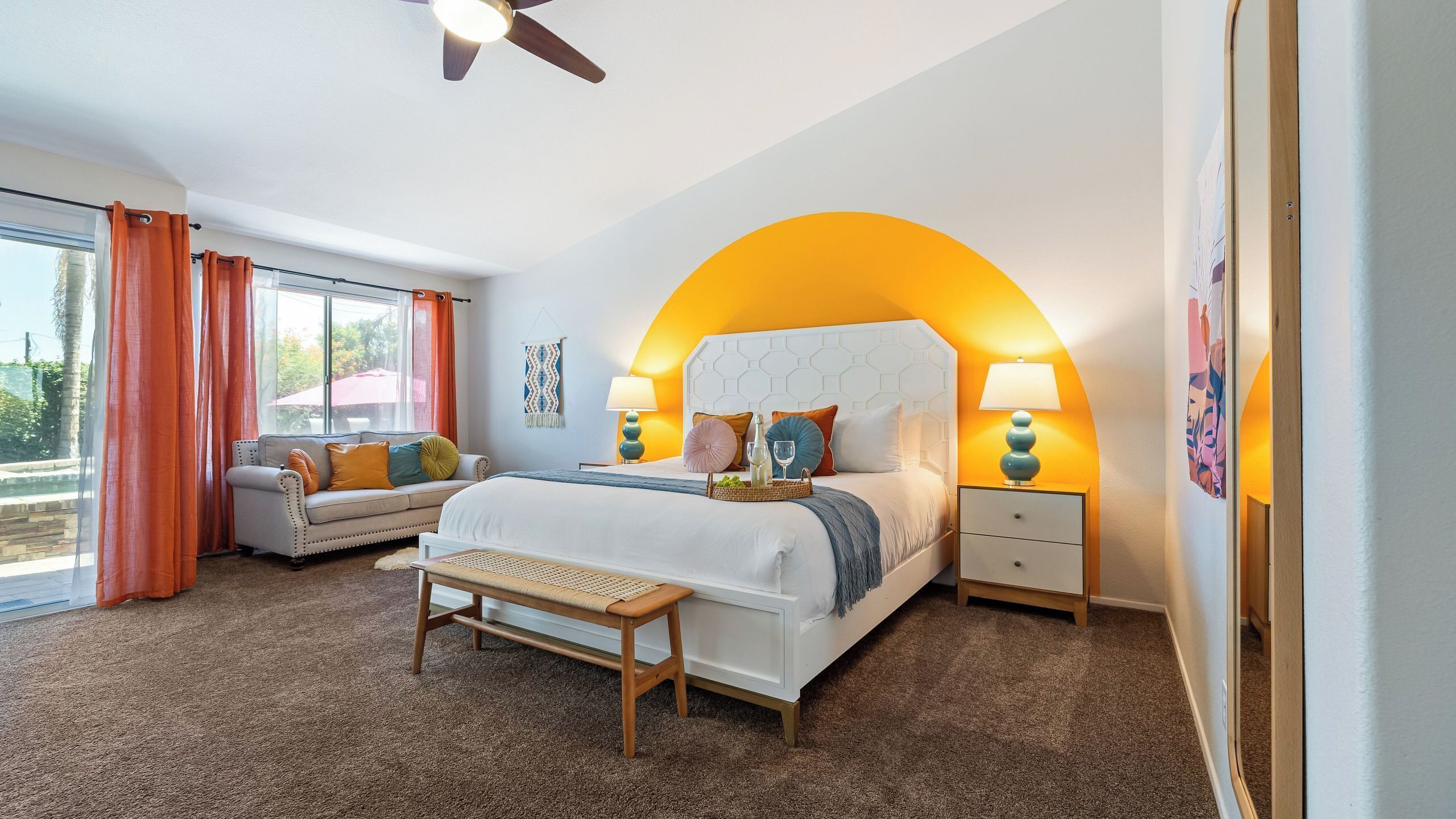 A bedroom with a bed, bedside tables, a bench, a ceiling fan, and a window with curtains.