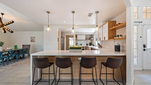 Une cuisine moderne dotée d’un îlot central, de tabourets de bar, de luminaires suspendus et d’un coin repas avec une table et des chaises.