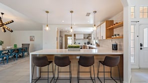 A modern kitchen with a central island, bar stools, pendant lighting, and a dining area with a table and chairs.