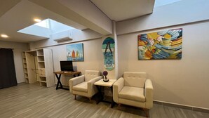 A room with a wooden floor, a desk with a laptop, two chairs, a small table with a vase, and artwork on the walls. - Hermoso estudio en Cozumel 5 (Cozumel)