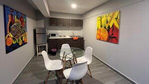 A modern kitchen with dark cabinets, a microwave, and a sink. There is a dining area with a glass table and white chairs. - Hermoso estudio en Cozumel 5 (Cozumel)