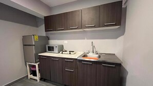 A compact kitchen with dark wooden cabinets, a stainless steel sink, a microwave, and a refrigerator. - Hermoso estudio en Cozumel 5 (Cozumel)