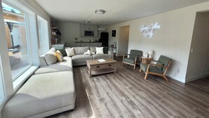 A modern living room with a sectional sofa, a coffee table, and two armchairs. A kitchen is visible in the background, and a neon sign reads "Good Vibes Only." - Convenient modern 2br home, 5 mins from airport. (Tukwila)