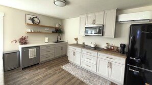 A modern kitchen with white cabinets, a black refrigerator, a microwave, and a dishwasher. - Convenient modern 2br home, 5 mins from airport. (Tukwila)
