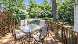 Une terrasse en bois avec une table et des chaises en verre, entourée d’une clôture en bois et d’arbres.