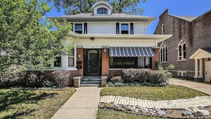 Une maison à deux étages avec un porche à l’avant, une façade en briques et un petit jardin agrémenté d’un chemin menant à l’entrée.