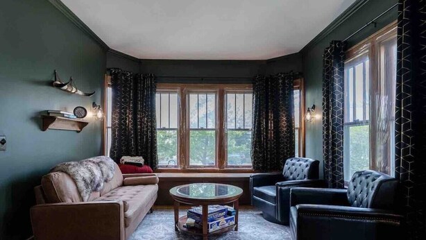 Un salon chaleureux avec un canapé, des fauteuils, une table basse en verre et une fenêtre avec des rideaux.