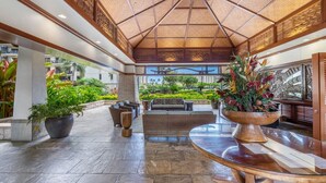 A spacious lobby with a high ceiling, a central seating area, and large potted plants.
