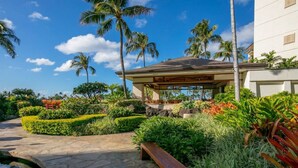 A resort with a covered outdoor seating area, lush tropical landscaping, and a clear blue sky.