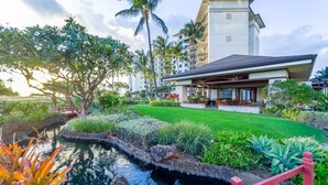 A hotel with a pool, lush greenery, and a red bridge.