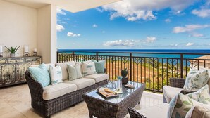 A balcony with a wicker sofa, a glass coffee table, and a view of the ocean.