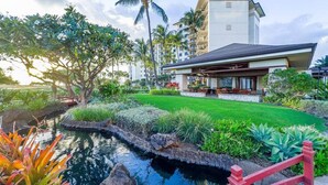 Un hotel moderno con un jardín bien cuidado, un pequeño estanque y un puente rojo.
