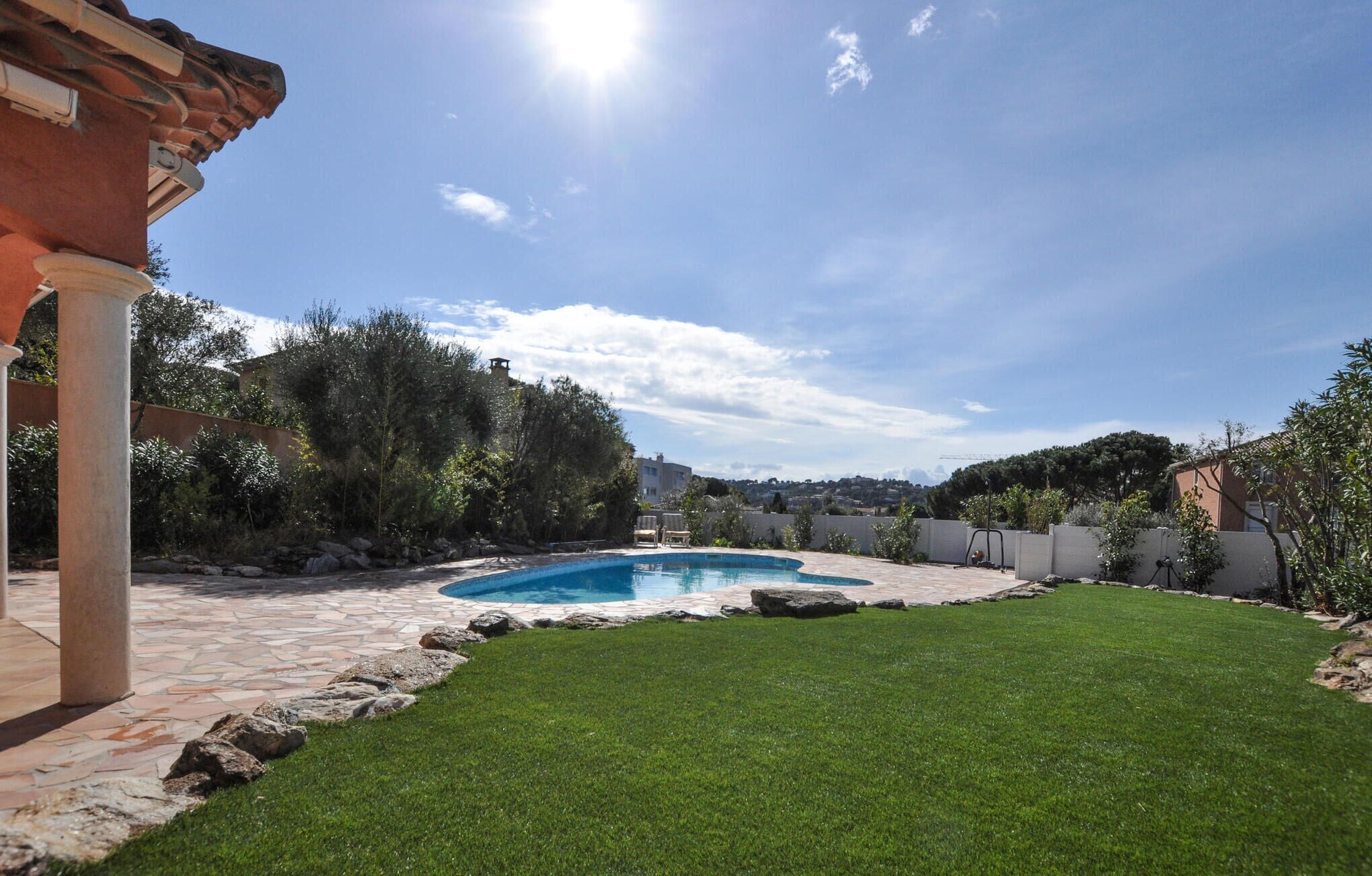A backyard with a swimming pool, a grassy lawn, and a stone patio.