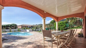 En täckt uteplats med pool, utomhusmöbler och utsikt över ett bostadsområde.