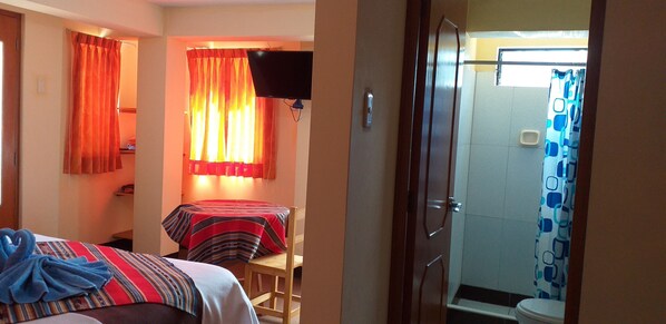 A hotel room with two beds, a TV, a shower with a curtain, and a small table.