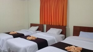 A hotel room with two single beds, each with white linens and a brown headboard. There is a large orange curtain above the beds.