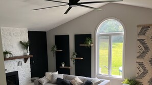 A modern living room with a grey sectional sofa, a fireplace, and a dining area with a wooden table and chairs. - Upper Rideau - “The West” Resort (Portland)