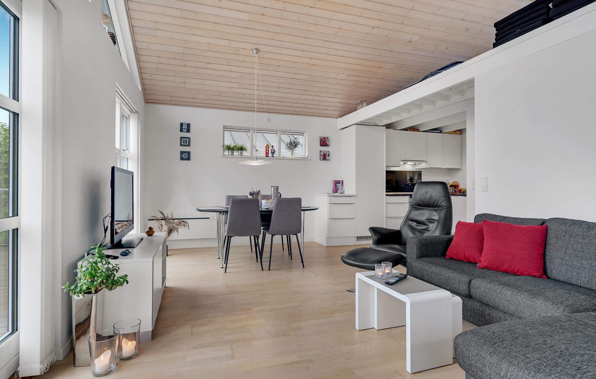 A modern living room with a grey sofa, a dining area with a table and chairs, and a kitchen in the background.