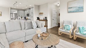 A modern living room with a sofa, chairs, a coffee table, and a kitchen in the background.