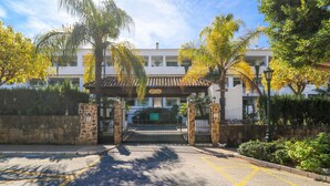 A gated entrance with a cobblestone pathway leading to a building with a tiled roof and multiple balconies. - Bahia Real apartment with large terrace (Marbella)