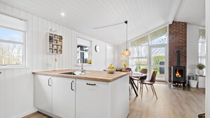 Une cuisine moderne avec des meubles blancs, un îlot central en bois et une cheminée en briques.