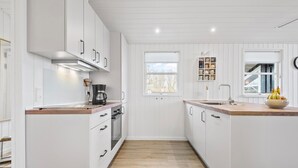 Une cuisine moderne avec des meubles blancs, un plan de travail en bois, une machine à café et un saladier rempli de fruits.