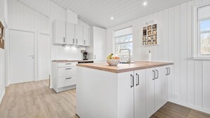 Une cuisine moderne avec des meubles blancs, un plan de travail en bois et un saladier rempli de fruits.