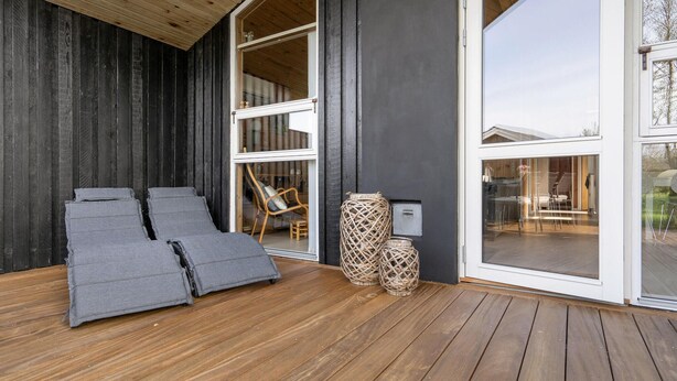Une terrasse extérieure moderne avec un plancher en bois, un ensemble de fauteuils de jardin gris et un panier en osier.
