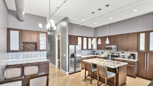 A modern kitchen with dark wooden cabinets, a stainless steel refrigerator, a built-in microwave, and a granite countertop island with bar stools.
