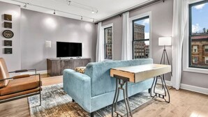 A modern living room with a sofa, a coffee table, a TV, and a city view through large windows.