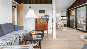 Una sala moderna con un sofá, una mesa de centro con una revista, un mueble de madera y un comedor con sillas y una mesa.