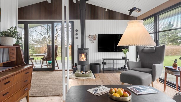 Una sala de estar moderna con chimenea, un sillón cómodo, una mesa de comedor con fruta y un televisor montado en la pared.