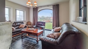 A spacious living room with leather sofas, a wooden coffee table, and a large window with curtains.