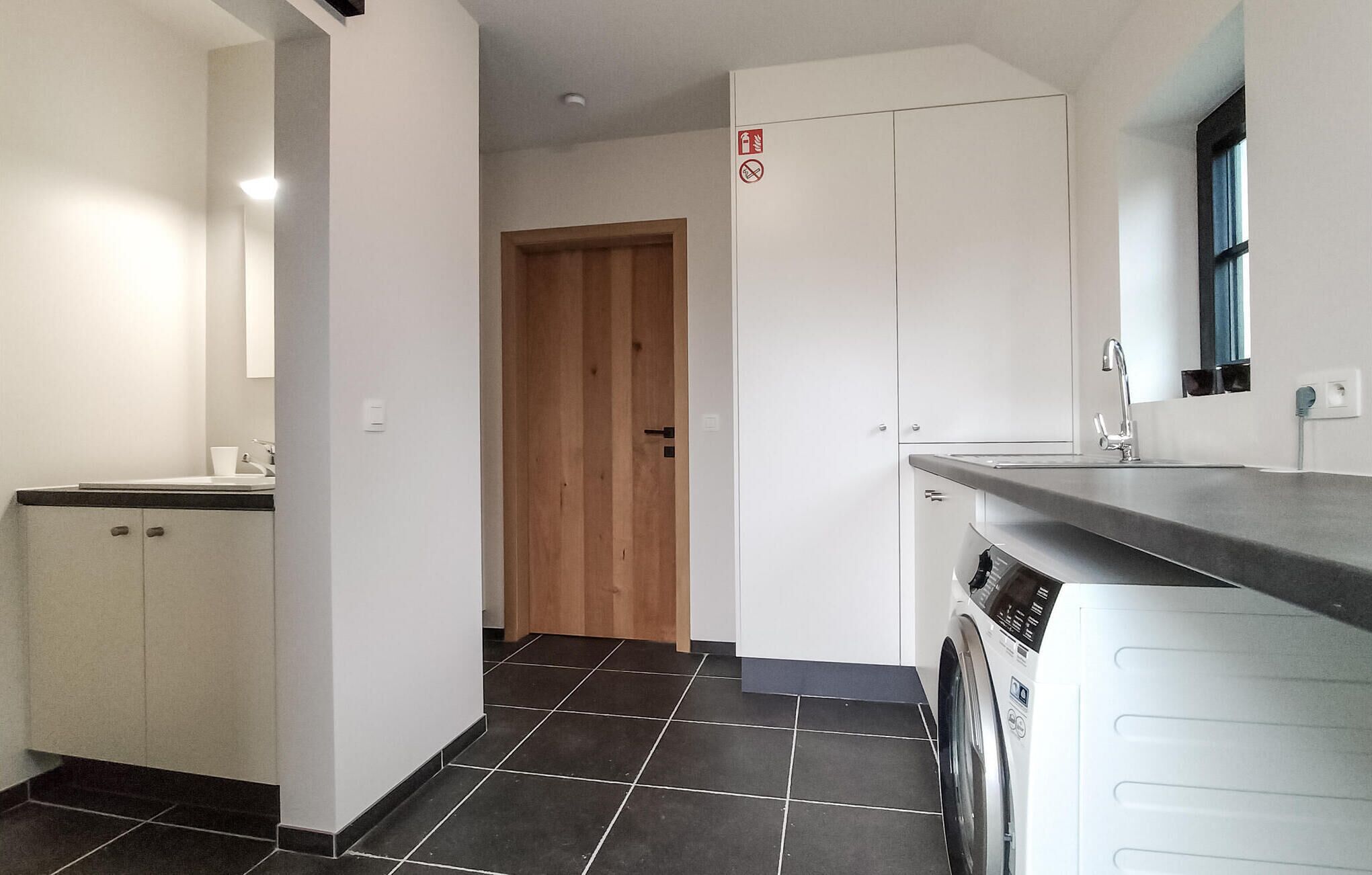 A modern kitchen with a built-in washing machine, a wooden door, and a tiled floor.