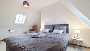 A bedroom with a large bed, a chair, a small table, and a hanging light fixture.