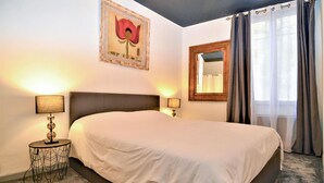 A hotel room with a large bed, two bedside lamps, a framed artwork above the bed, a mirror on the wall, and a window with curtains. - Beautiful home in Sommières with WiFi (Sommières)
