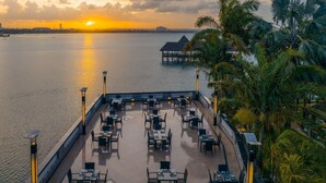 Um restaurante à beira-mar com mesas ao ar livre e vista para o pôr do sol sobre a água.