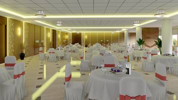 Un salón de banquetes con mesas redondas, sillas blancas con cintas rojas y candelabros.