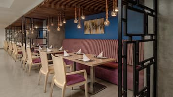 Un restaurant avec des tables et des chaises en bois, un banc rouge rembourré et des luminaires suspendus.