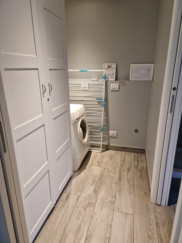 Une buanderie équipée d’un lave-linge, d’un étendoir et d’un panneau de commande fixé au mur.