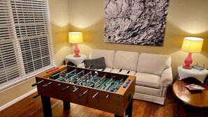 A living room with a foosball table, a sofa, two lamps, and a painting on the wall.