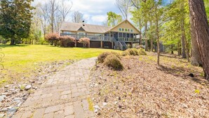 A two-story house with a covered porch, a stone pathway, and a wooded area.